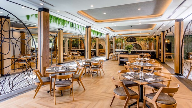 Un restaurante moderno con muebles de madera, plantas verdes y un suelo con estampado de espiga.