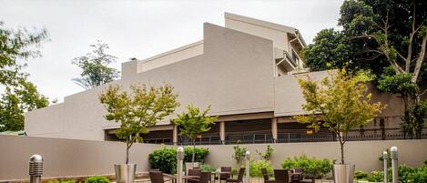 Un patio con mesas al aire libre, un edificio moderno y jardines ajardinados.
