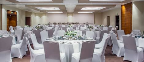Un salón de banquetes con mesas redondas, sillas blancas y centros de mesa florales.