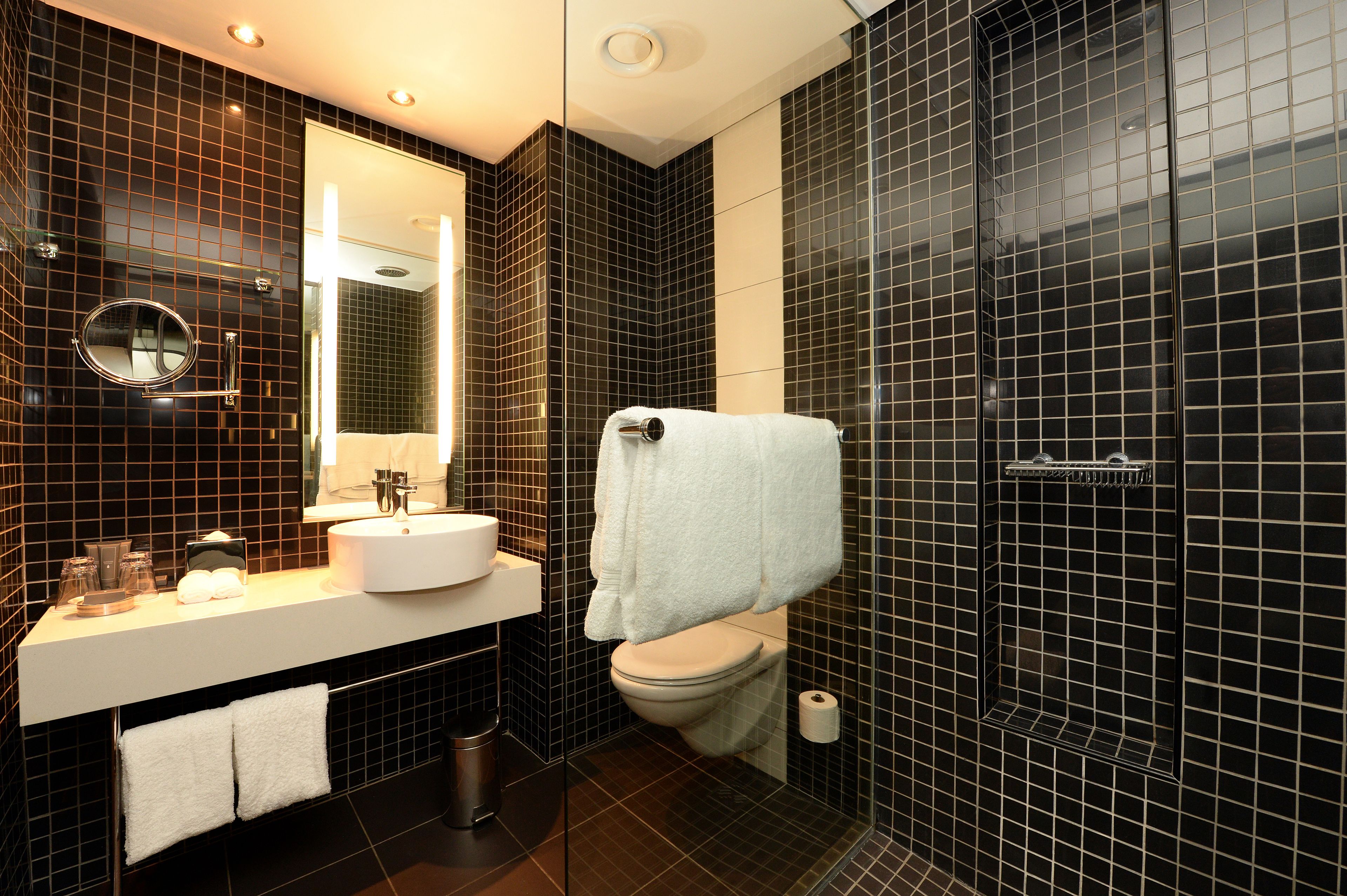 Un baño moderno con pared de azulejos negros, un lavabo blanco, un espejo y un inodoro.