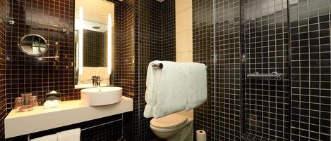 Un baño moderno con pared de azulejos negros, un lavabo blanco, un espejo y un inodoro.
