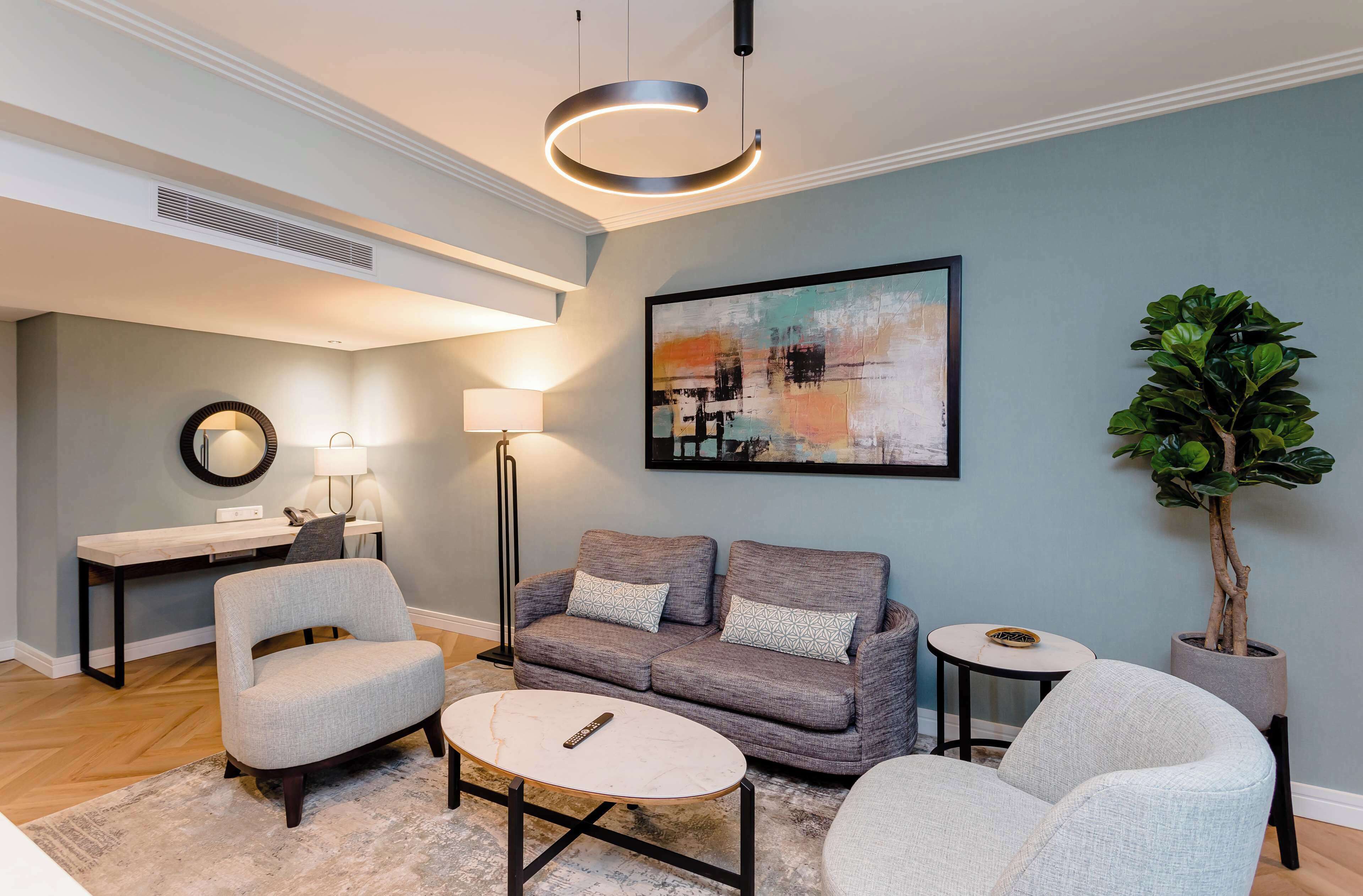 Un salon moderne avec un canapé gris, deux fauteuils, une table basse, un bureau et une plante en pot.