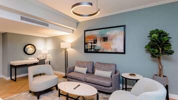 A modern living room with a grey sofa, two armchairs, a coffee table, a desk, and a potted plant.