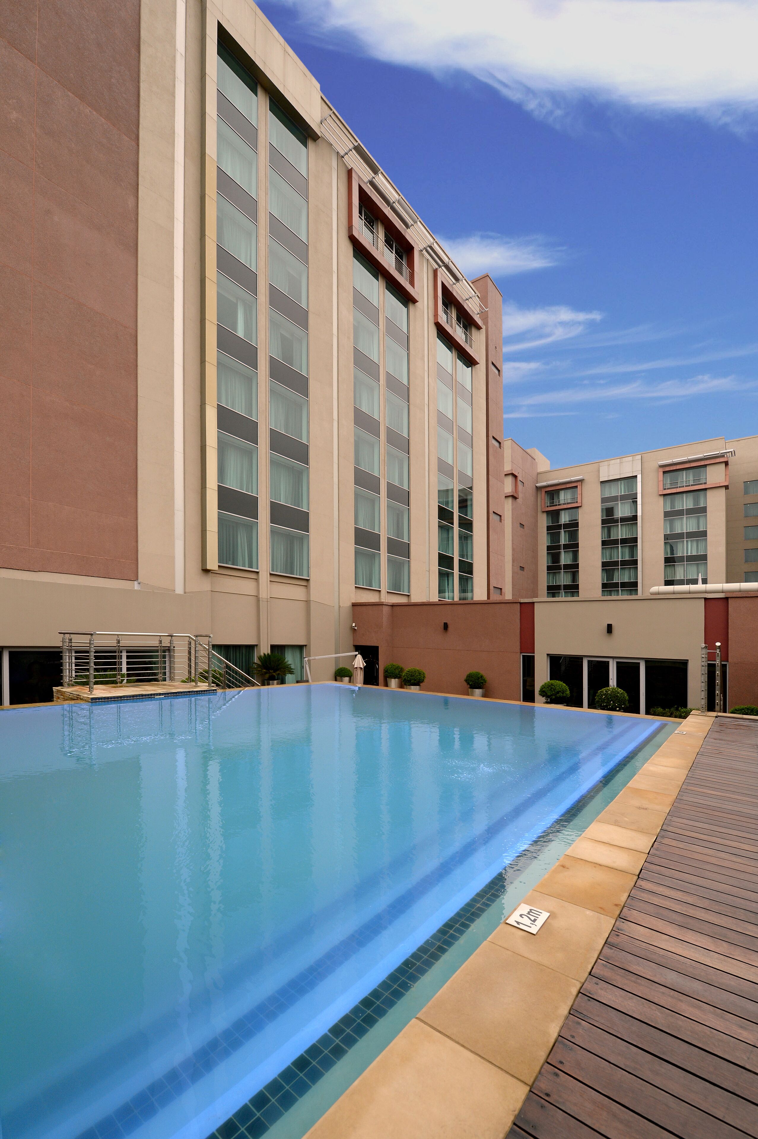 A modern hotel with a large indoor swimming pool, a covered patio area, and a large building facade with large windows.