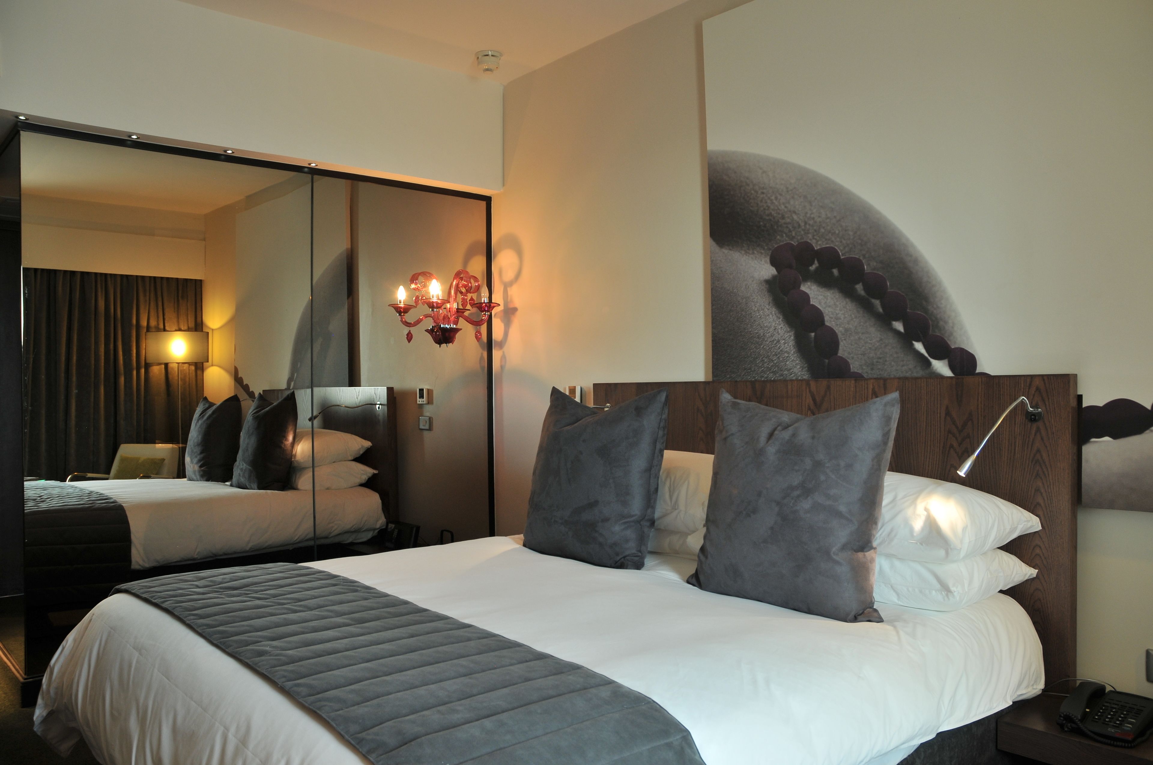 Une chambre d’hôtel avec un grand lit, un miroir, une lampe fixée au mur et un téléphone sur la table de chevet.