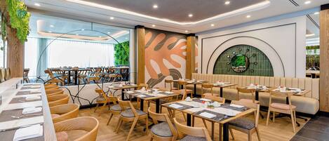 A modern restaurant with wooden tables and chairs, a large mural, and a circular green wall feature.