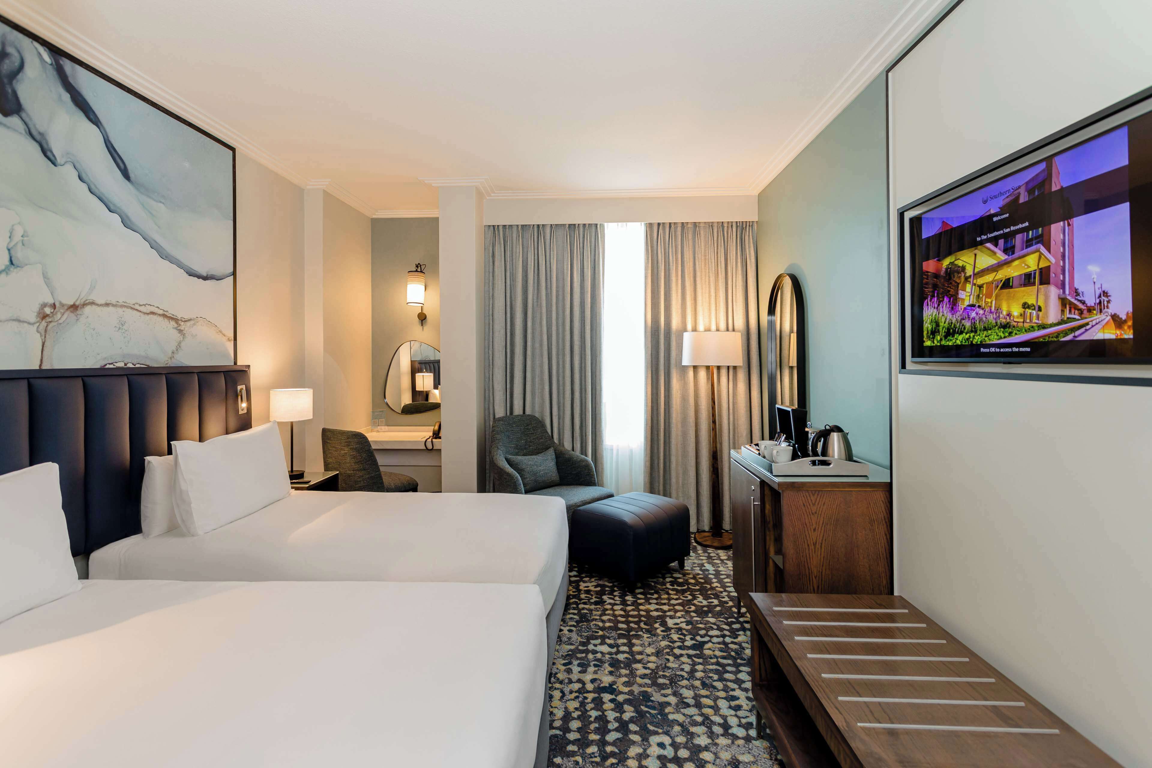 Una habitación de hotel con una cama grande, un escritorio con lámpara, una silla, un televisor y un cuadro en la pared.