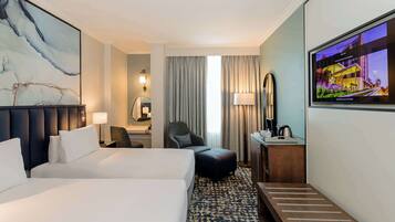 Una habitación de hotel con una cama grande, un escritorio con lámpara, una silla, un televisor y un cuadro en la pared.