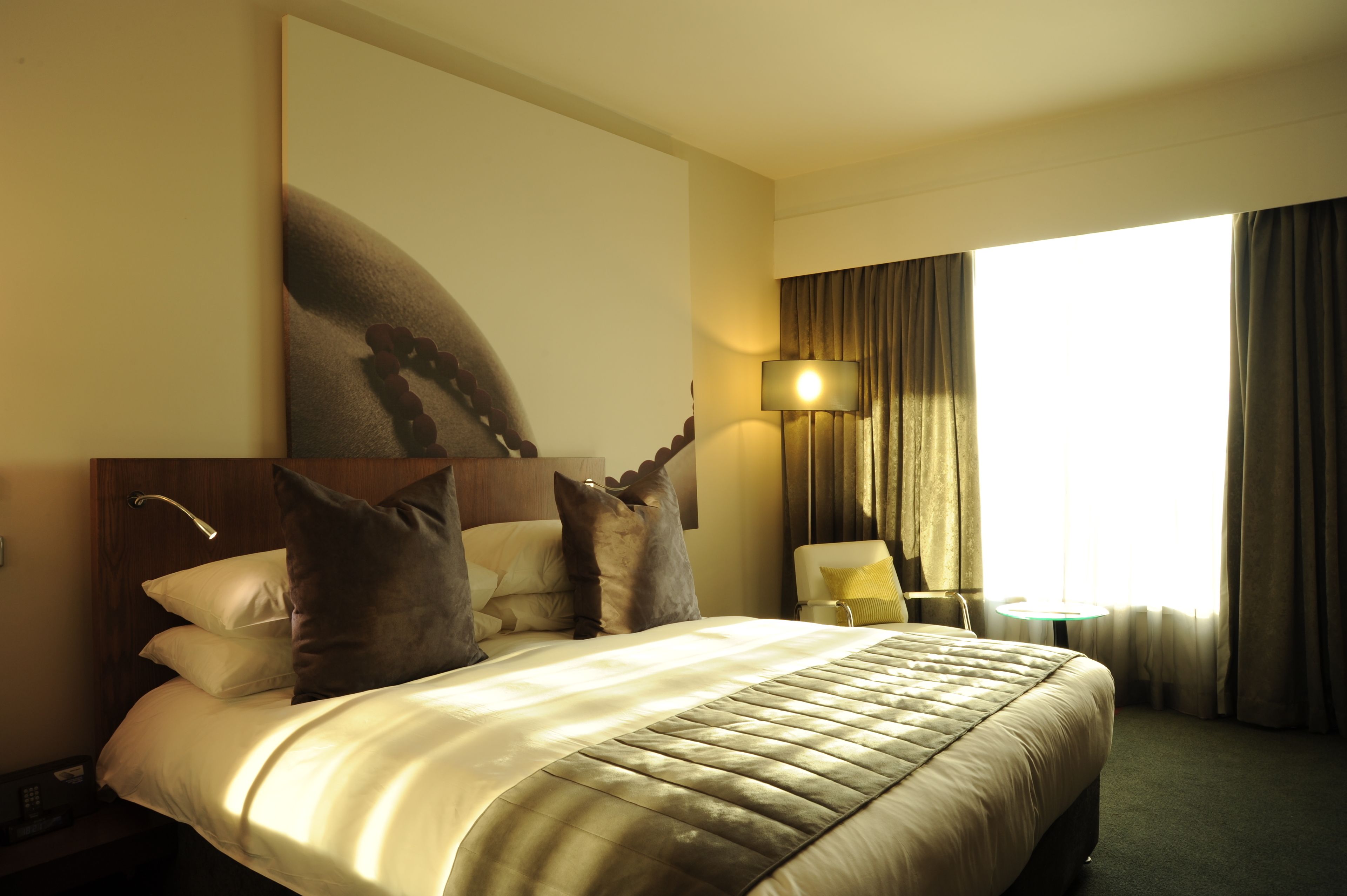 A hotel room with a large bed, a nightstand, a lamp, and a view of the outdoors.