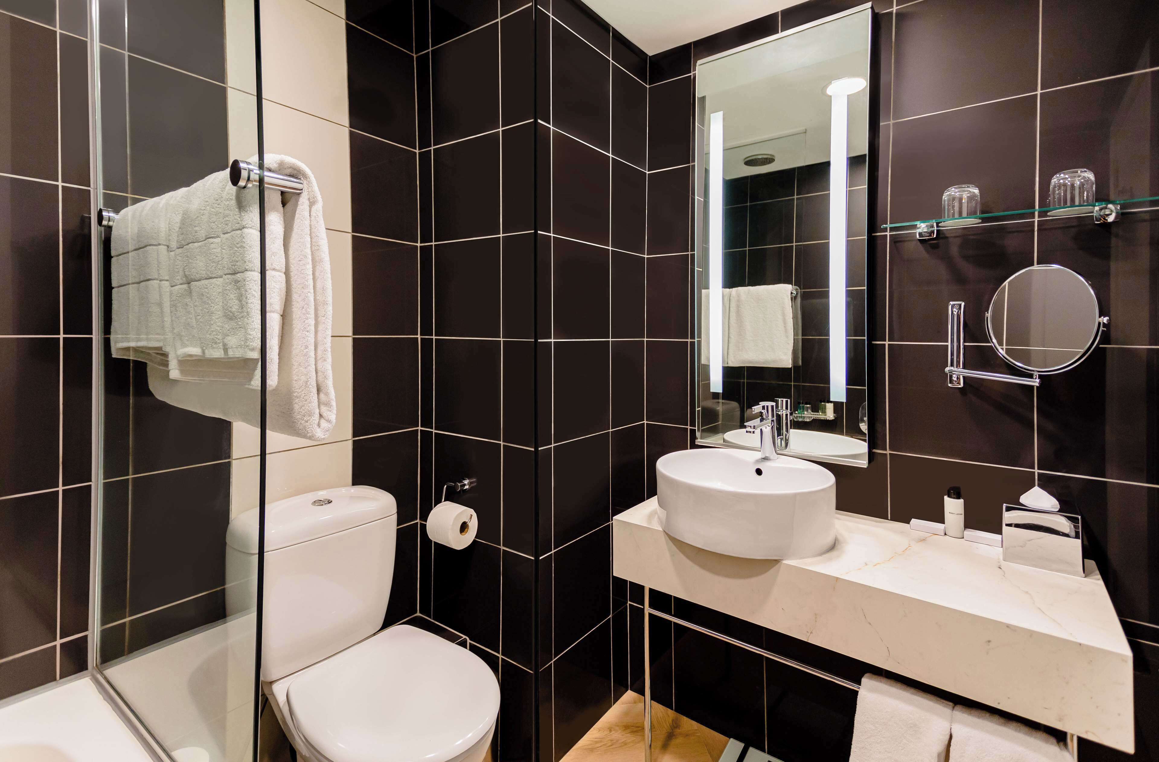 Een moderne badkamer met een douchecabine van glas, een wit toilet, een wastafel met spiegel en een handdoekrek.