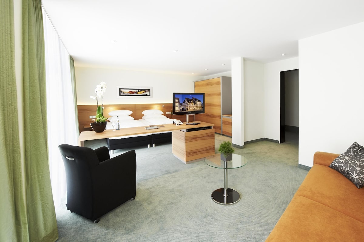 Una habitación de hotel moderna con una cama, un escritorio, un televisor, un sofá y una mesa de centro.