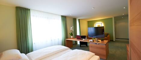 A hotel room with two beds, a desk with a laptop, a TV, and a plant.
