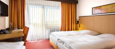 Habitación de hotel con dos camas, un escritorio con teléfono y gafas, una silla y un televisor en la pared.