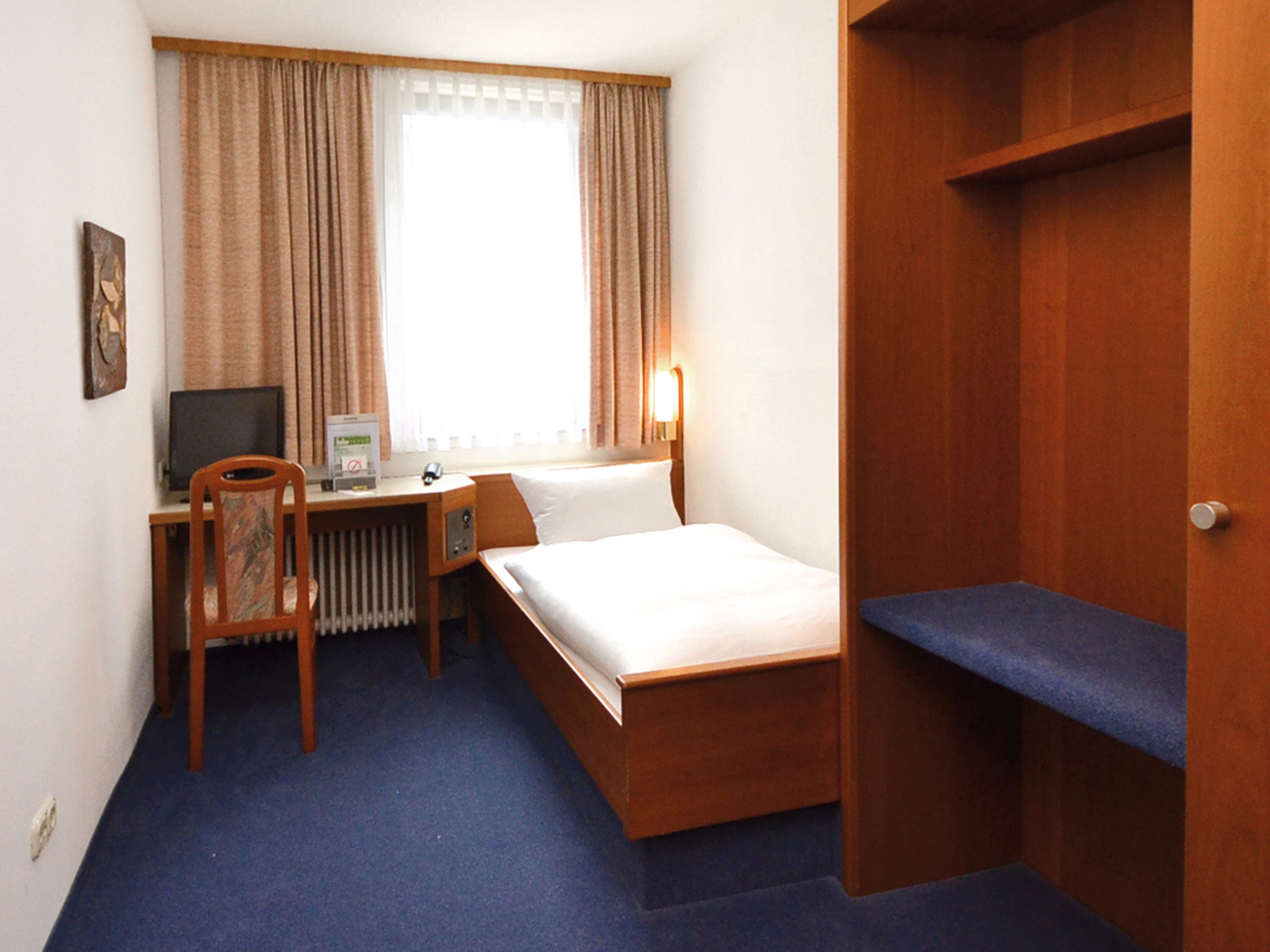 Habitación de hotel con cama, escritorio con computadora, una silla y ventana con cortinas.