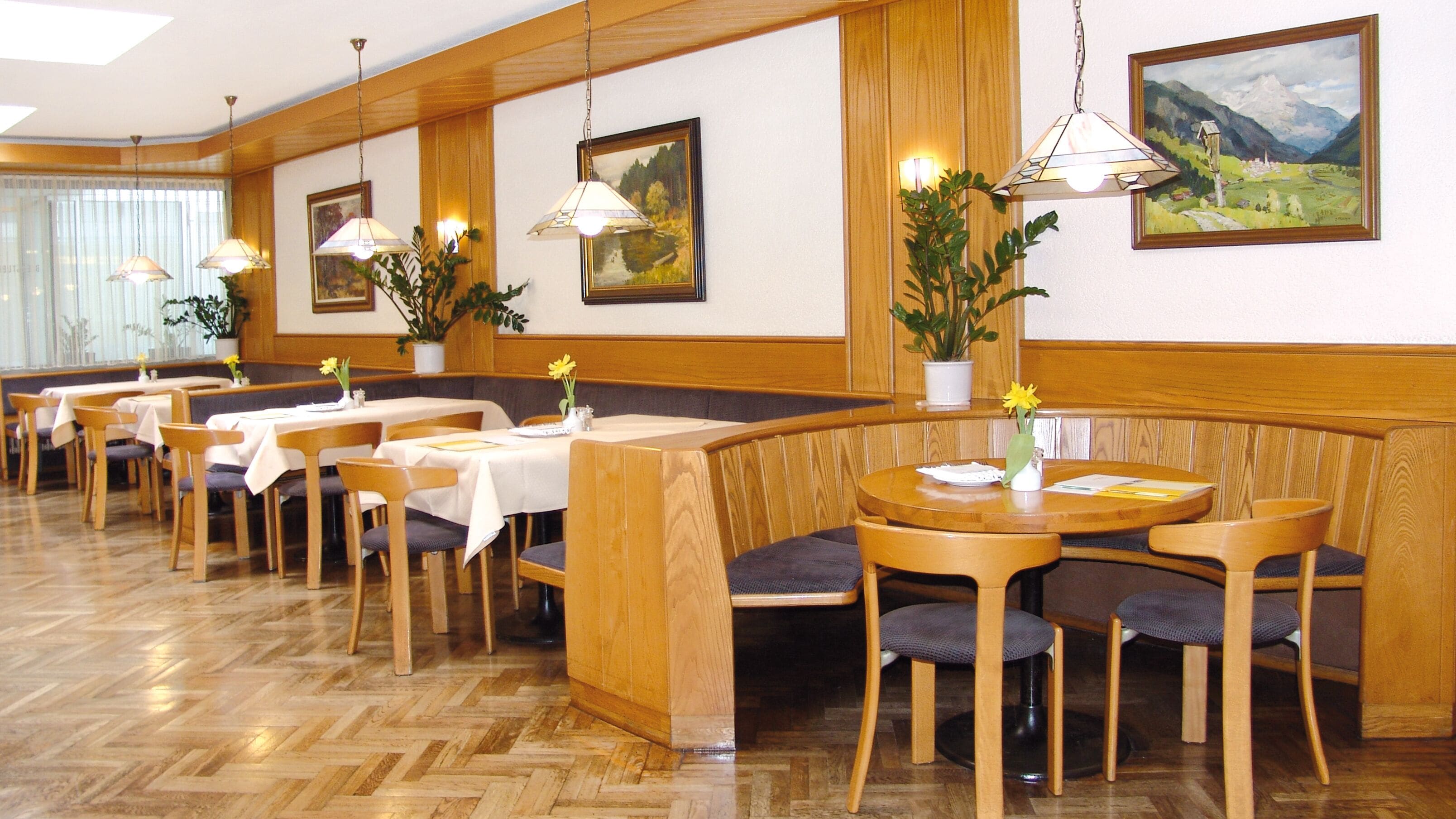 A restaurant with wooden booths and tables, potted plants, and framed paintings on the walls.