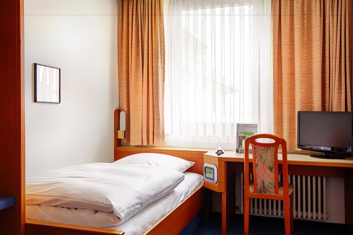 A hotel room with a single bed, a desk with a computer, and a chair.