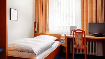 Una habitación de hotel con una cama individual, un escritorio con una computadora y una silla.