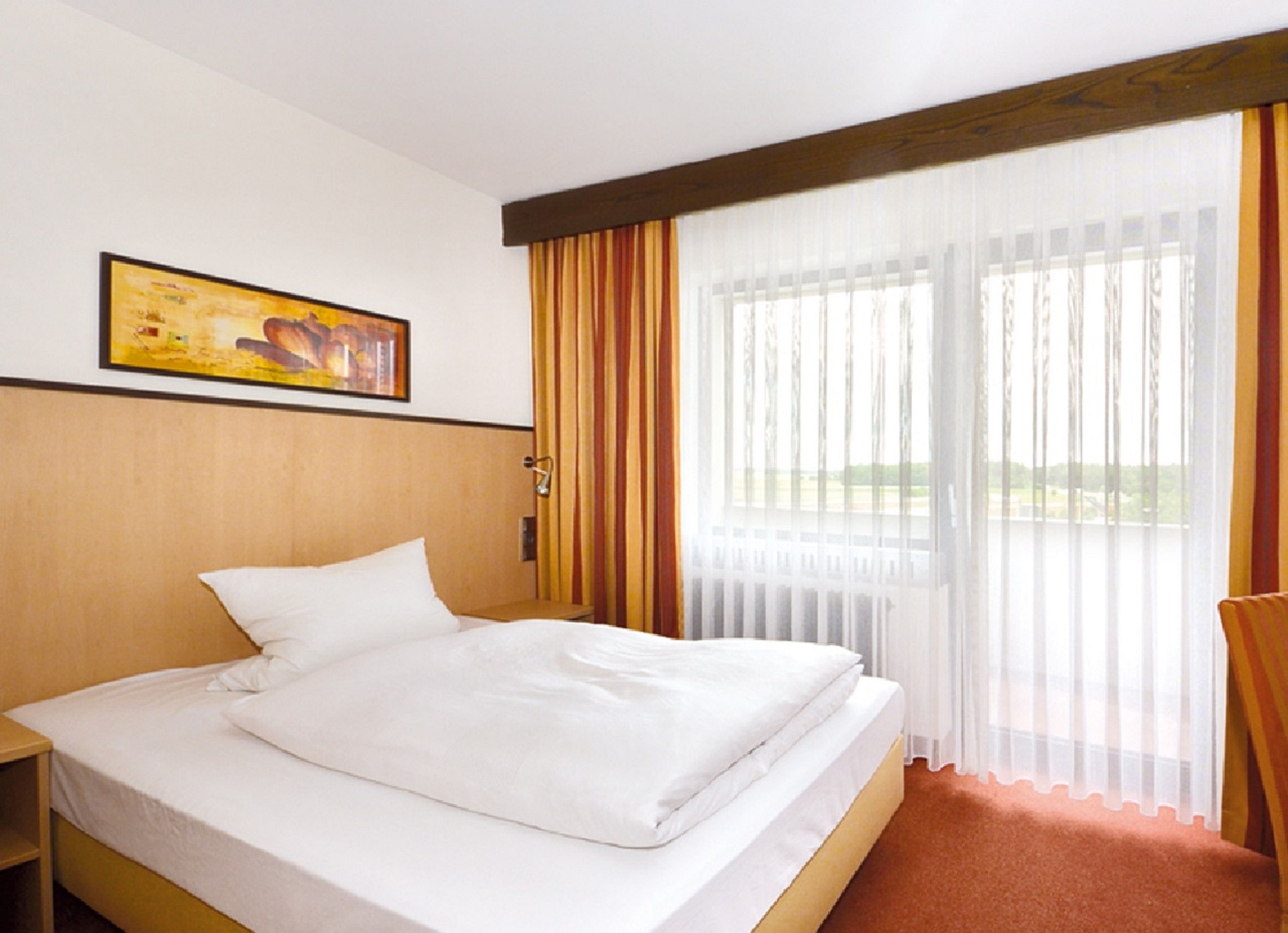 A hotel room with a bed, a painting on the wall, and a window with curtains.