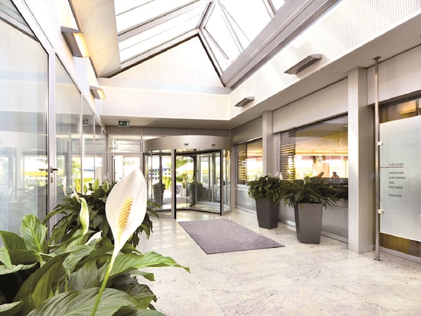 Un hall d’entrée moderne avec une entrée en verre, des plantes en pot et un sol en marbre.