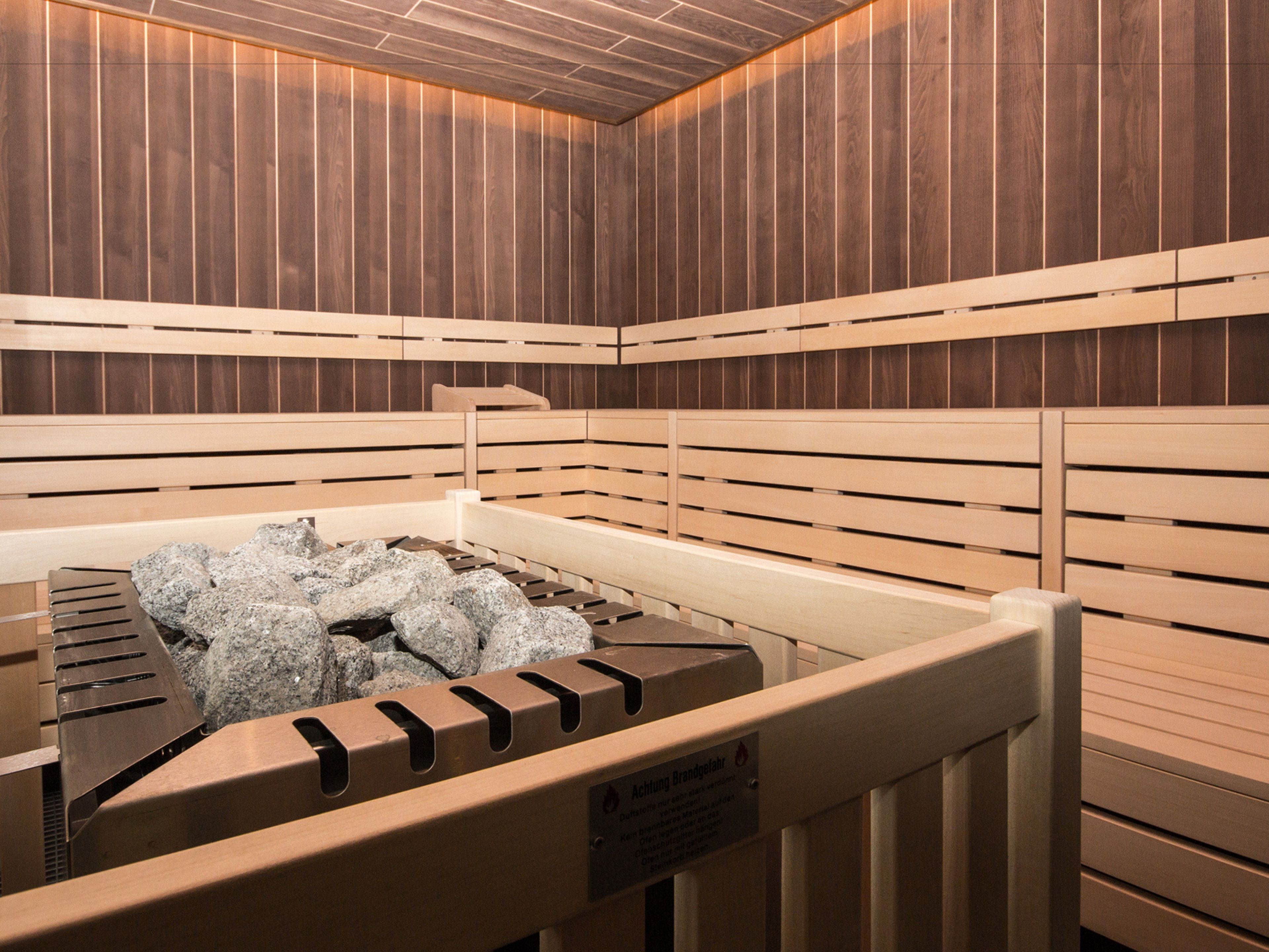 A sauna with wooden walls and benches, a heated floor, and a sign indicating the sauna is heated by brand fuel.