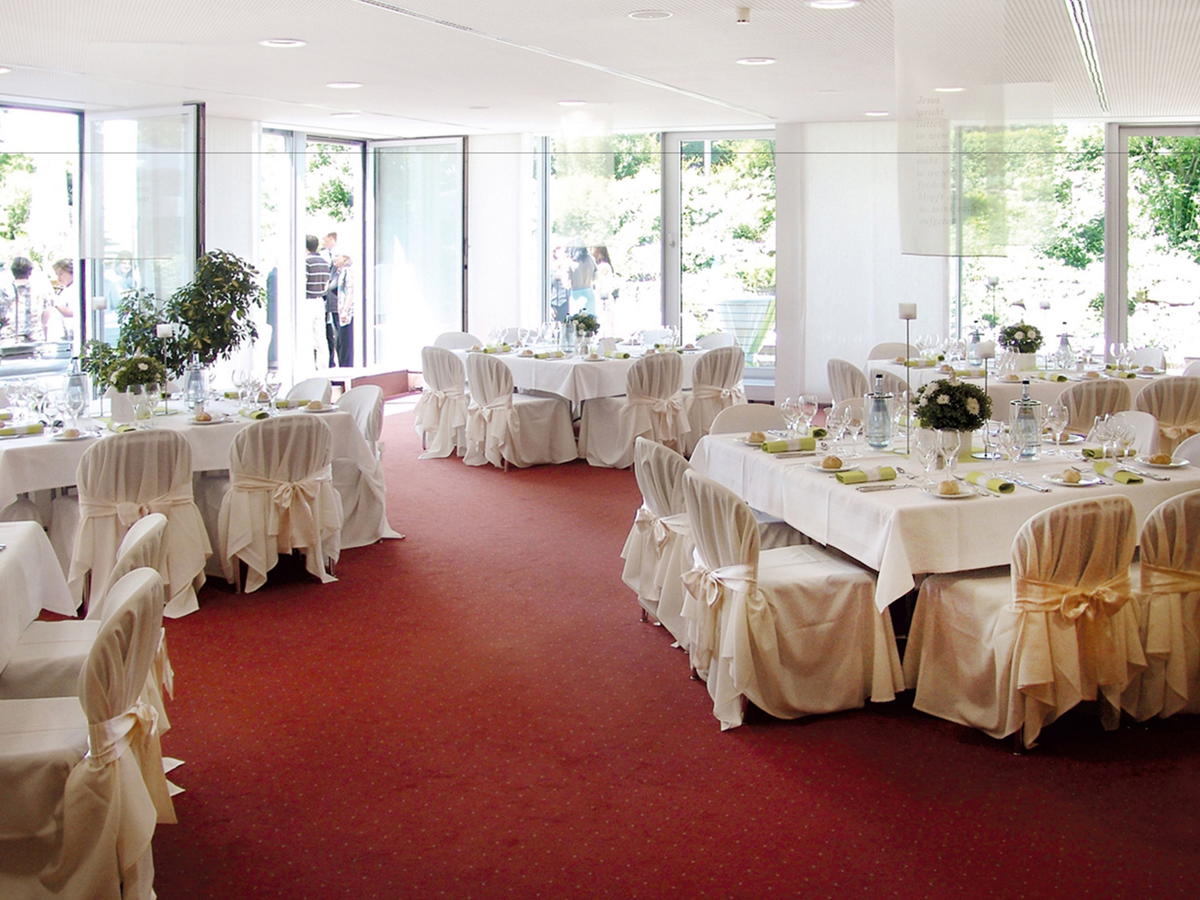 A banquet hall with tables set for a formal event, featuring white tablecloths and chairs with white coverings.