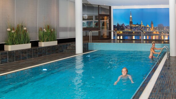 Una piscina interior con un mural de un paisaje urbano al fondo.