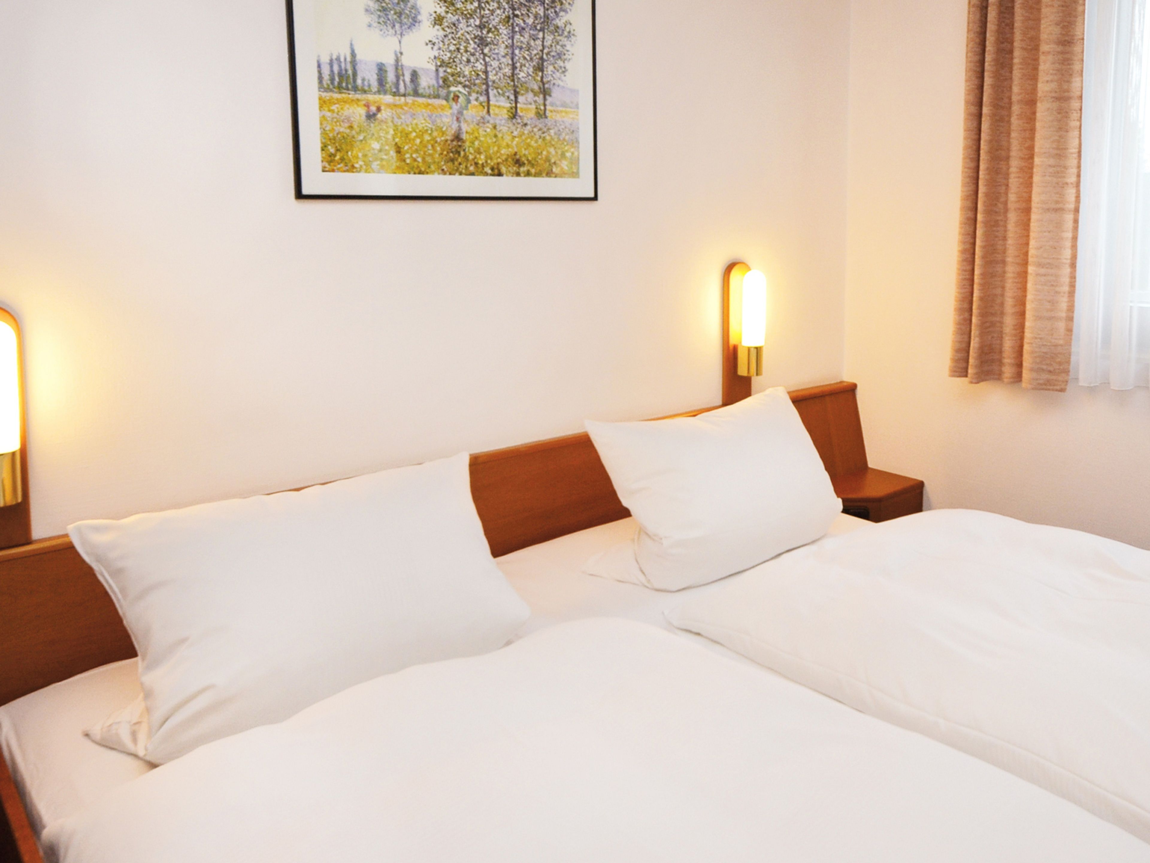 Een hotelkamer met een tweepersoonsbed, twee nachtkastjes, een bijzettafeltje en een ingelijste foto aan de muur.