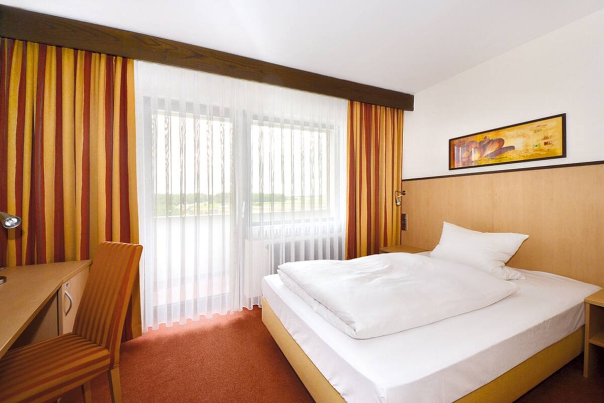 A hotel room with a bed, a desk, a chair, and a window with curtains.