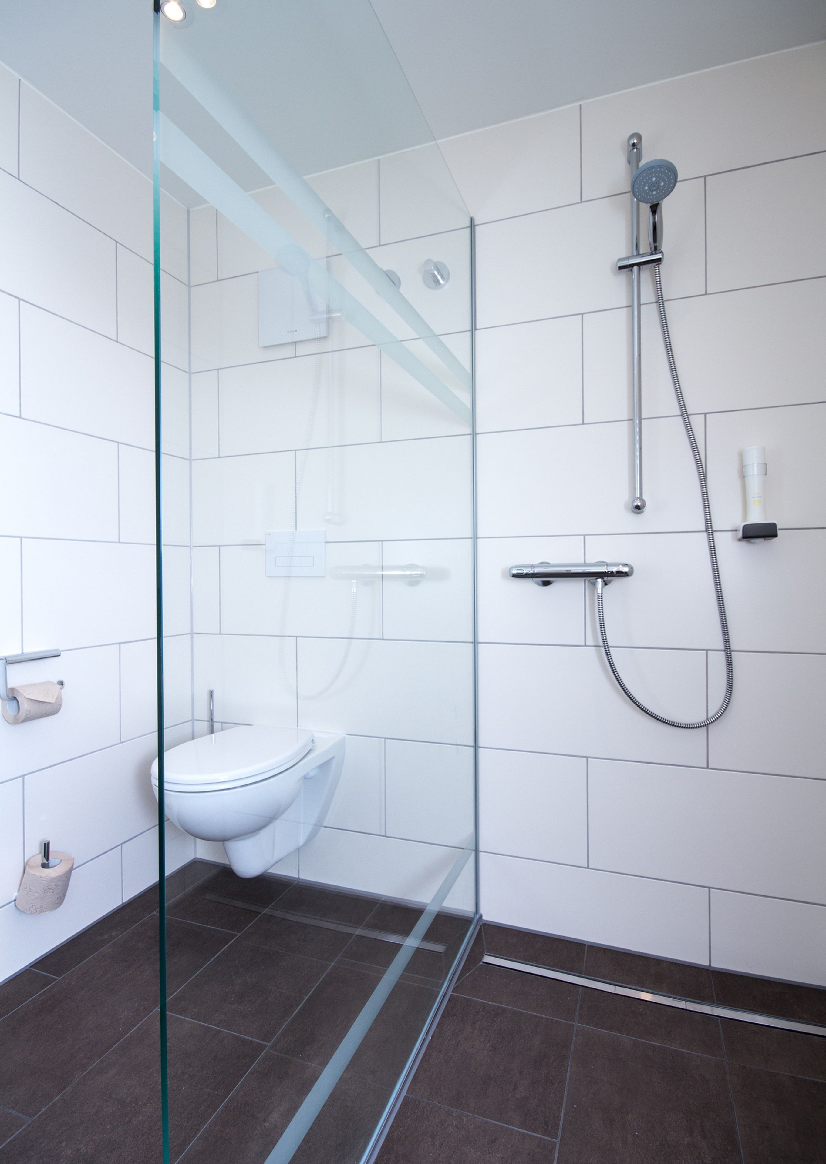 Un baño moderno con cabina de ducha de vidrio, inodoro blanco y ducha de mano.