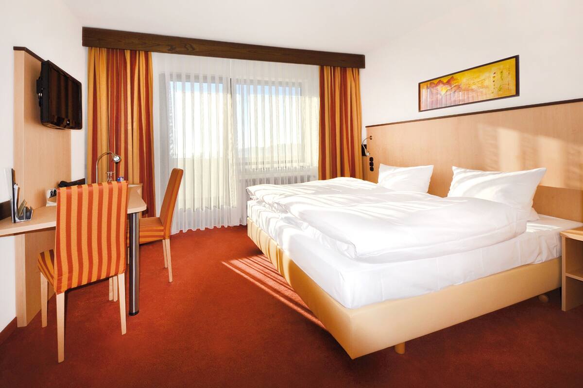 A hotel room with a large bed, a desk with a chair, a TV, and a window with curtains.