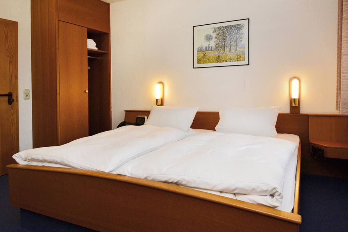 A double bed with wooden headboard and footboard, two bedside tables with lamps, a wardrobe, and a framed picture on the wall.