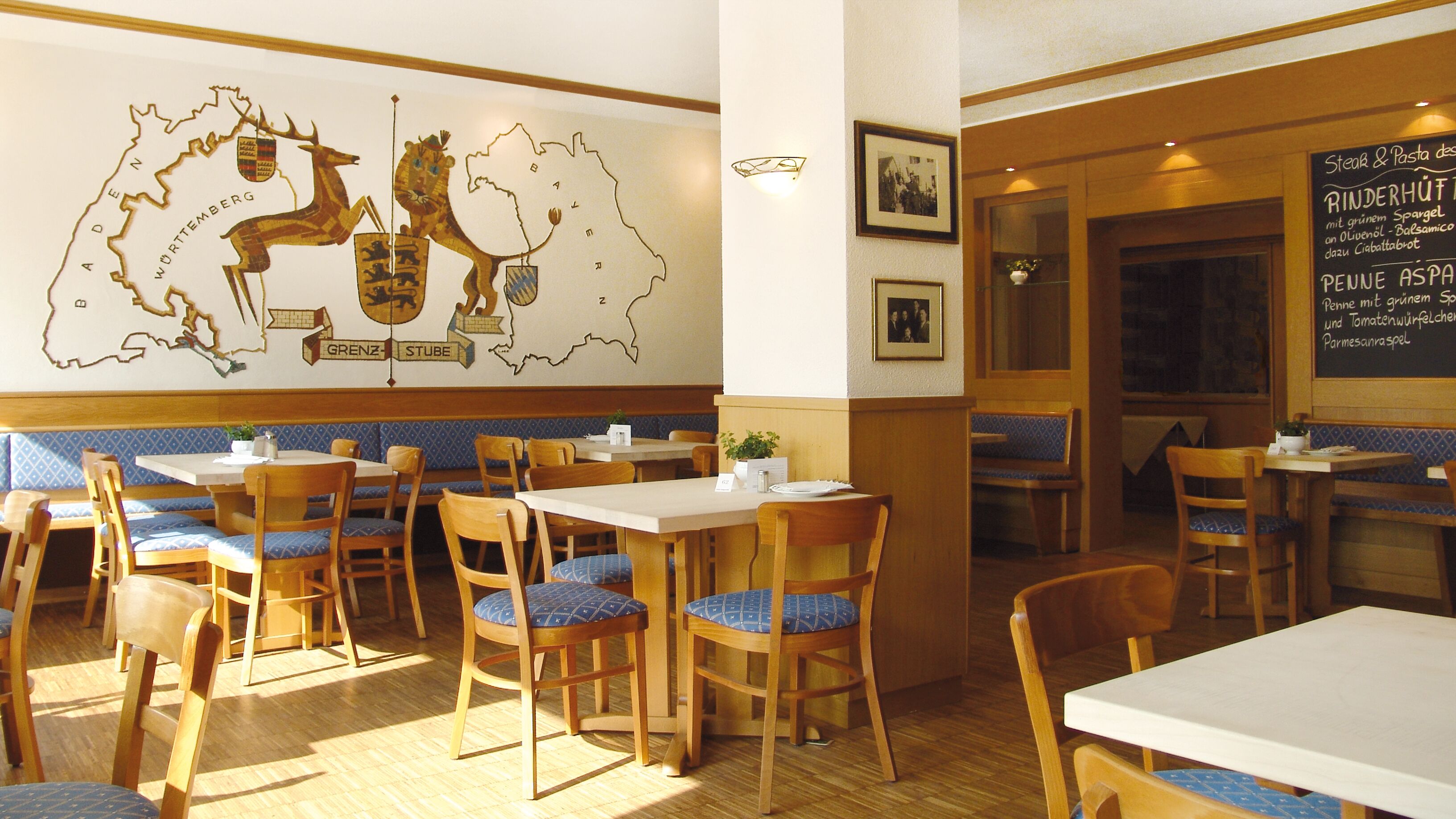 A restaurant interior with wooden tables and chairs, a wall mural, and a chalkboard menu.