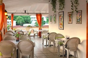 A restaurant with outdoor seating, white chairs, tables, and potted plants.