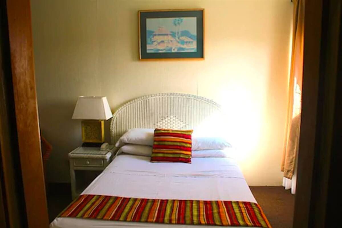 A hotel room with a bed, a nightstand, a lamp, and a framed picture on the wall.
