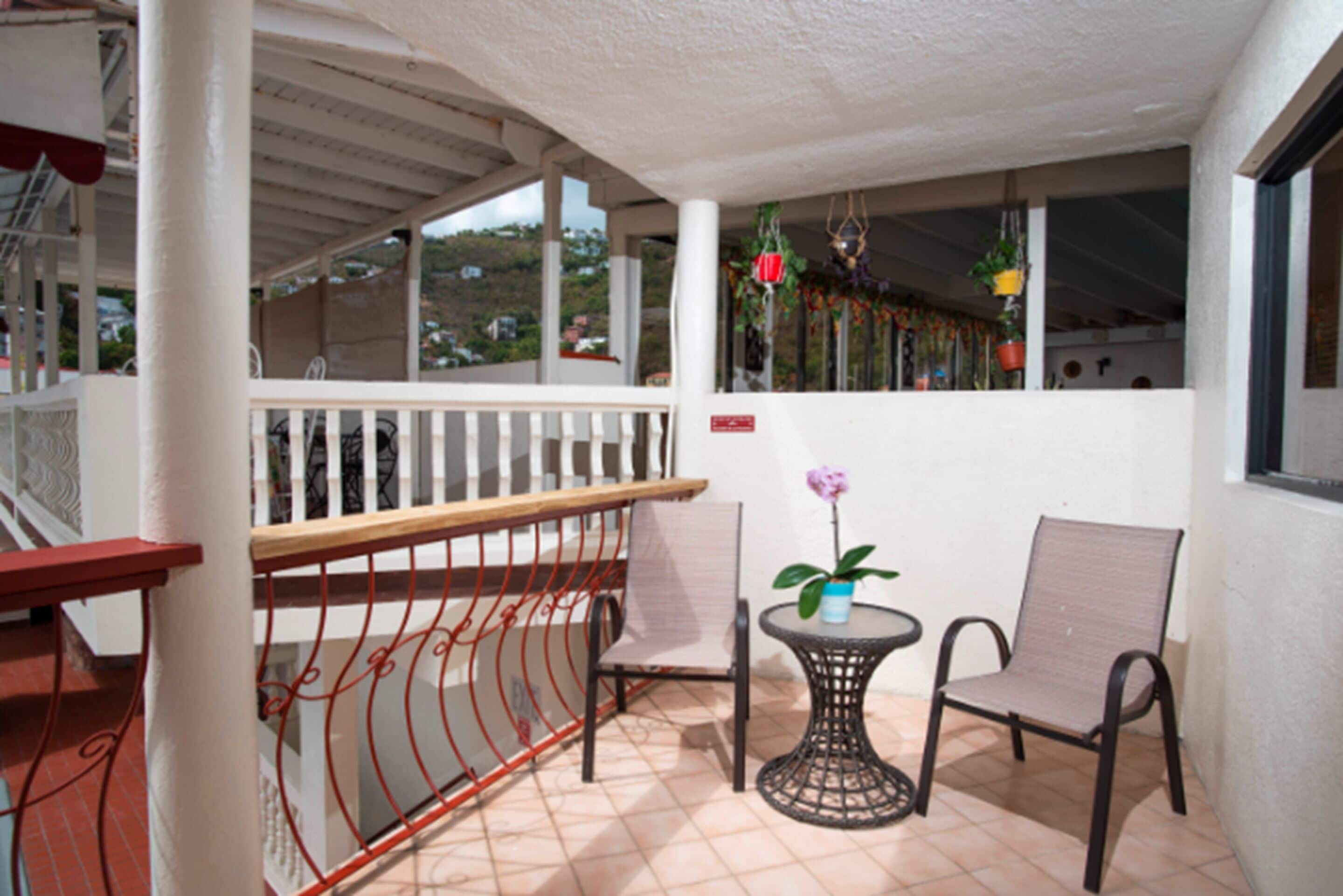 A balcony with a white railing, a small round table with a chair, and a potted plant.