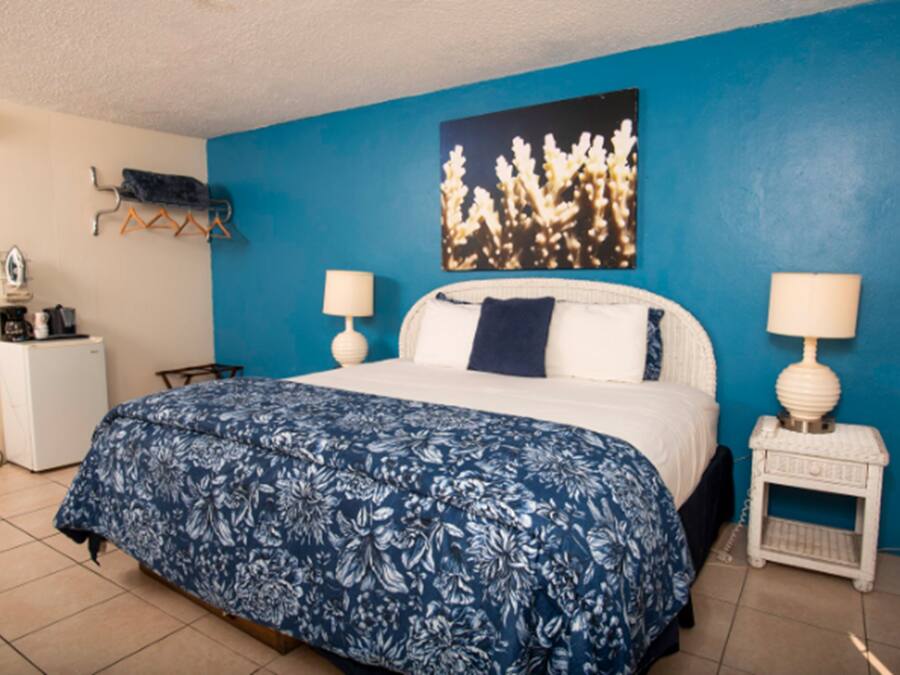 A bedroom with a bed, two bedside tables with lamps, a small desk, a heater, and a wall-mounted rack.