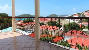 A balcony with a tiled floor and a metal railing, overlooking a residential area with red-roofed houses and greenery. - Bunker Hill Hotel (St. Thomas)