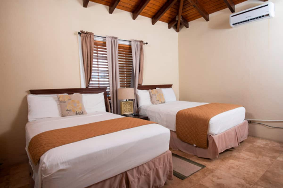 A hotel room with two beds, a nightstand, a lamp, and an air conditioning unit.