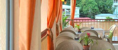 An outdoor dining area with wicker chairs and tables, orange curtains, and potted plants.