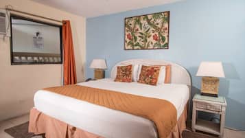 A neatly made bed with a white and brown bedspread, two bedside lamps, and a floral painting on the wall.