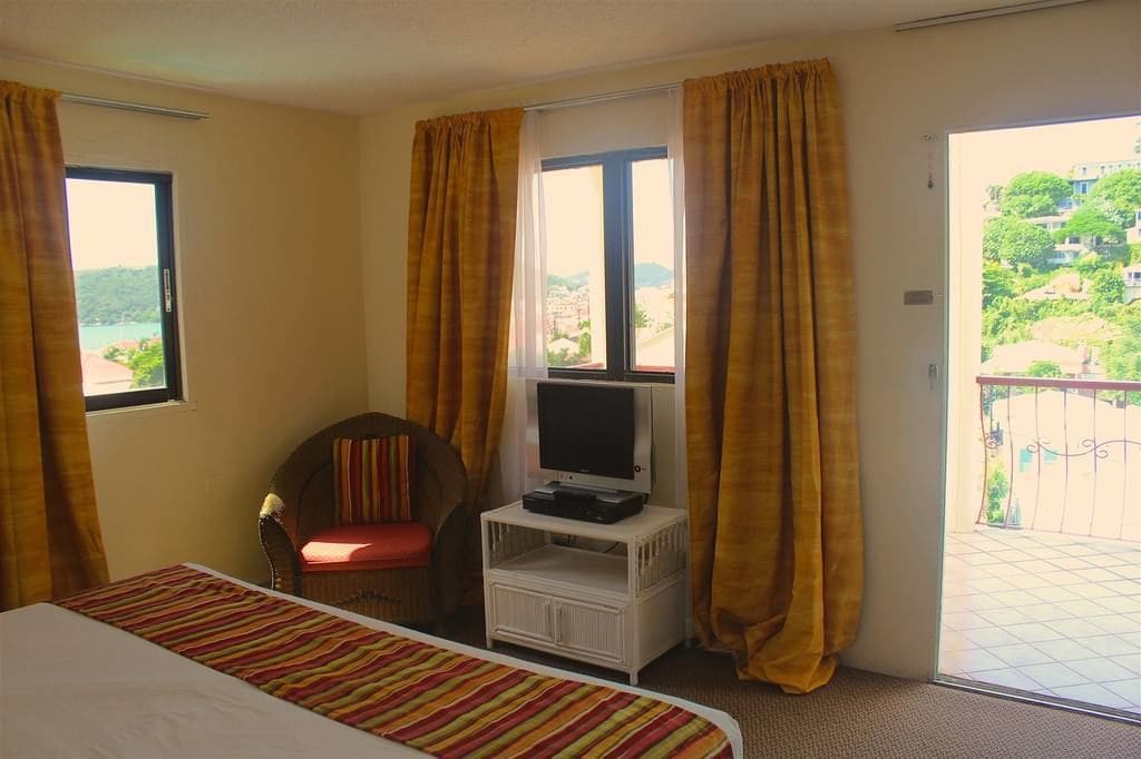 A hotel room with a bed, a television on a small stand, a chair, and a balcony with a view of a hillside.
