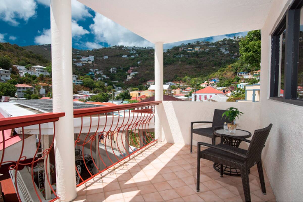 A balcony with a view of a hillside town, a table with chairs, and a potted plant.
