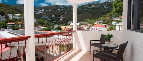Un balcón con vistas a un pueblo en la ladera, una mesa con sillas y una planta en maceta.