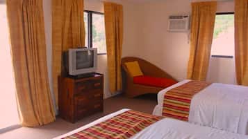 Habitación de hotel con dos camas, un televisor sobre una cómoda de madera y cortinas en las ventanas.