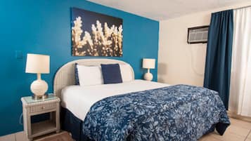 A hotel room with a bed, two bedside lamps, a wall-mounted air conditioner, and a window with curtains.