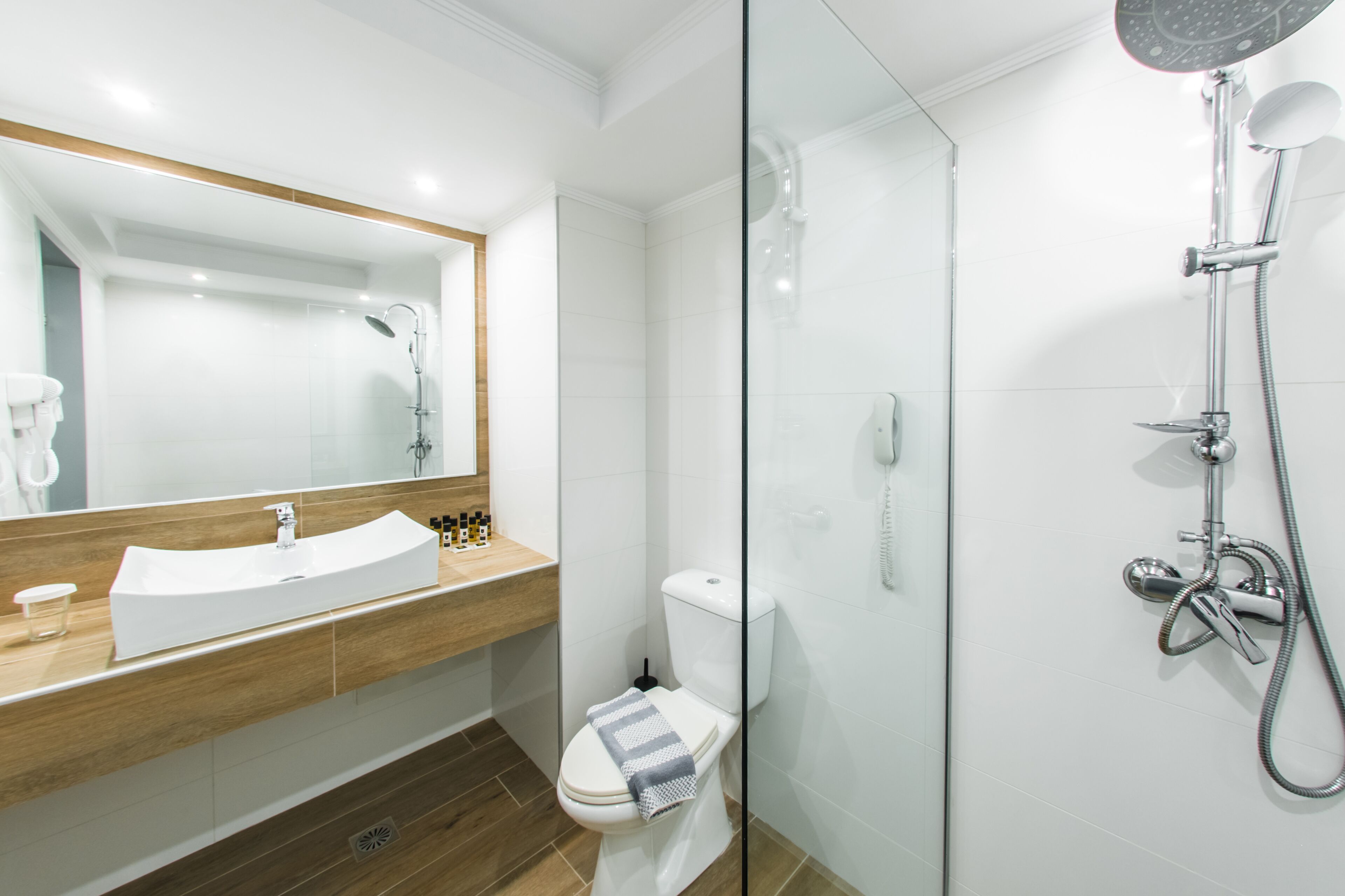 A modern bathroom with a glass-enclosed shower, a white sink with a wooden countertop, and a toilet with a towel on the seat.