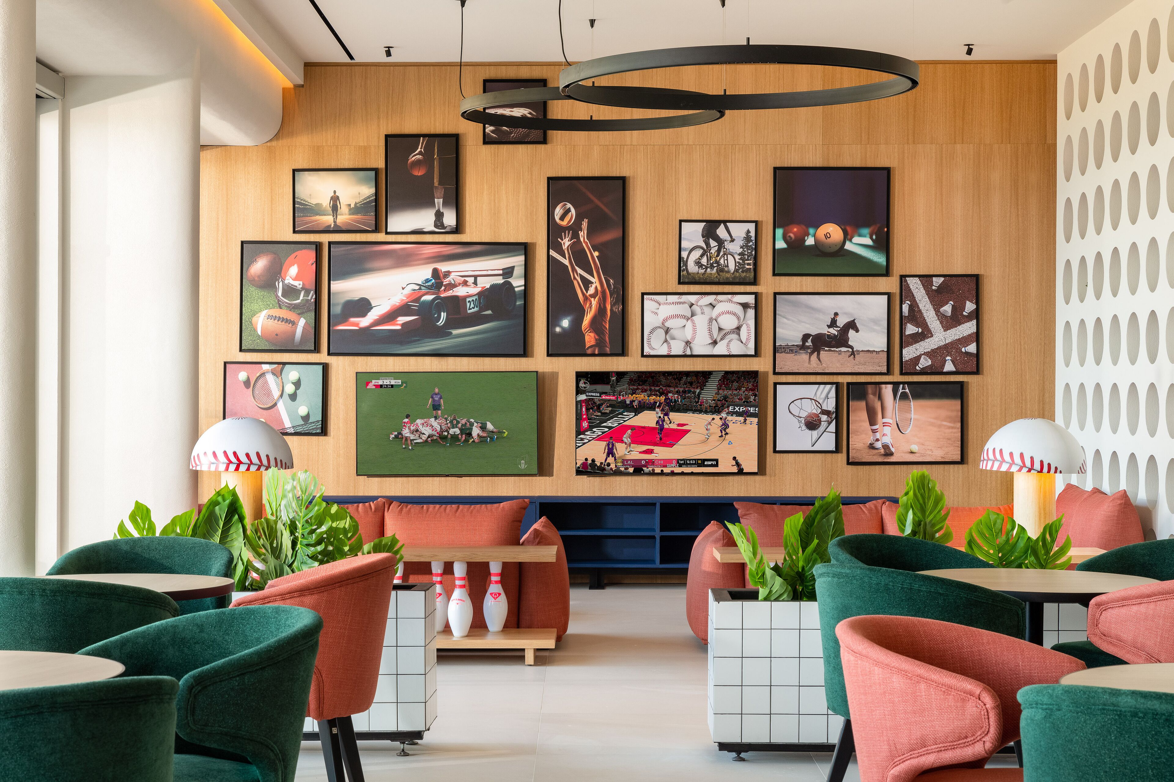 A modern lounge area with green and orange seating, a bowling lane, and various sports-themed wall art.