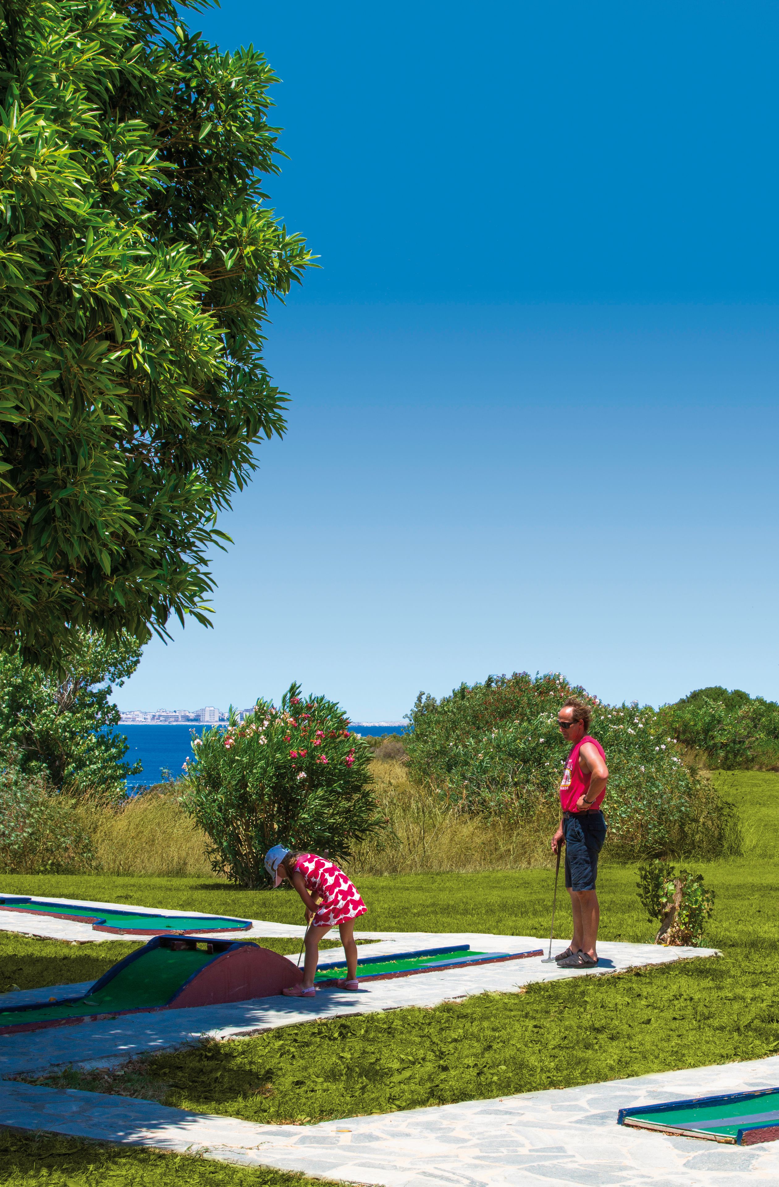 Un parcours de golf offrant une vue dégagée sur la mer, et une personne portant un t-shirt rose, debout sur un départ.