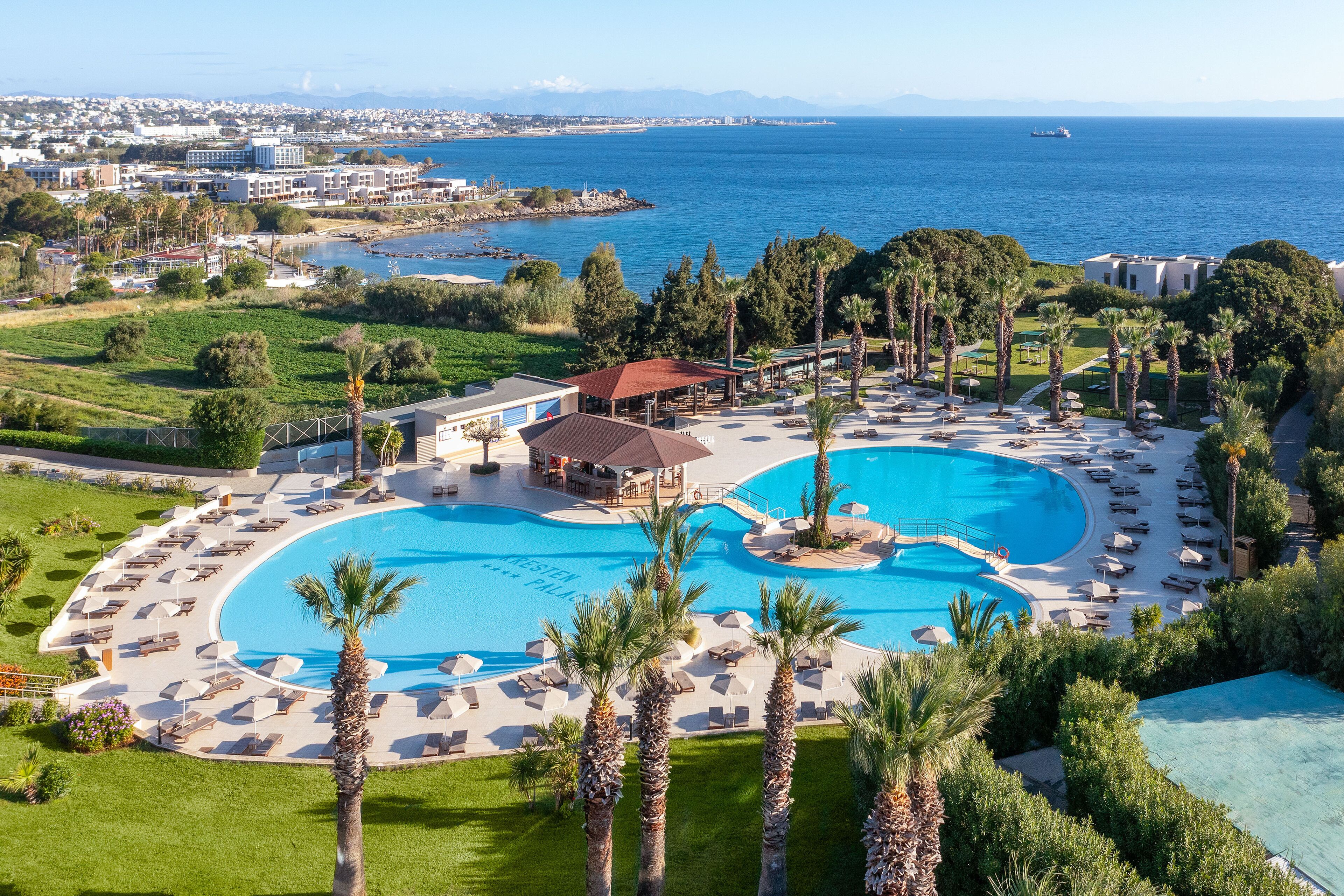 A resort with a large central pool, multiple lounge areas, and a view of the sea.