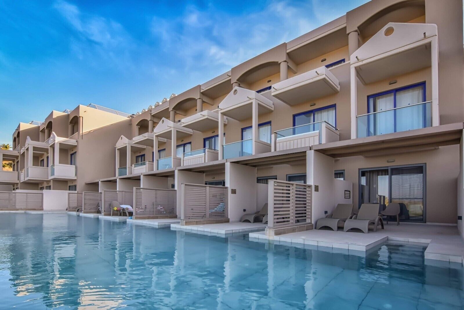 Un hotel con varios balcones, piscina y cielo azul despejado.